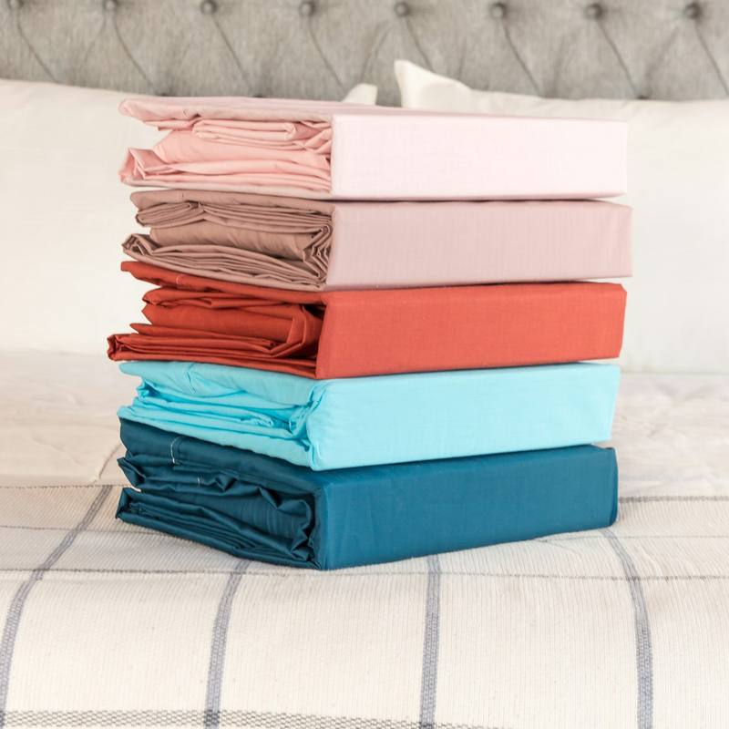 Stack of folded sheet sets in pink, coral and teal on a bed